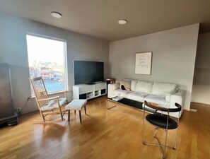 A living room with a white sofa, a wooden rocking chair, a black chair, a flat-screen TV, and a framed quote on the wall.