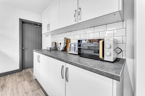A modern kitchen with white cabinets, a grey countertop, and a microwave. - Victoria House, Stoke on Trent (Stoke-on-Trent)