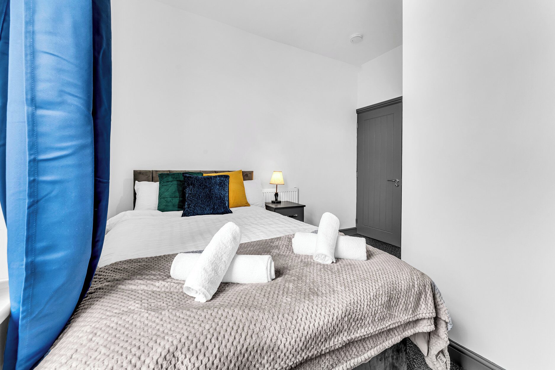 A hotel room with a bed, pillows, a nightstand, a lamp, and a wardrobe.