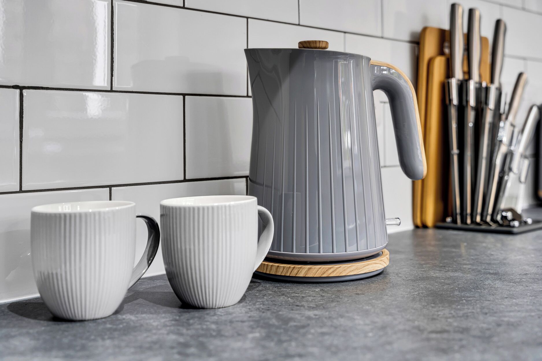 A kitchen counter with a gray kettle, two white mugs, and a knife block.