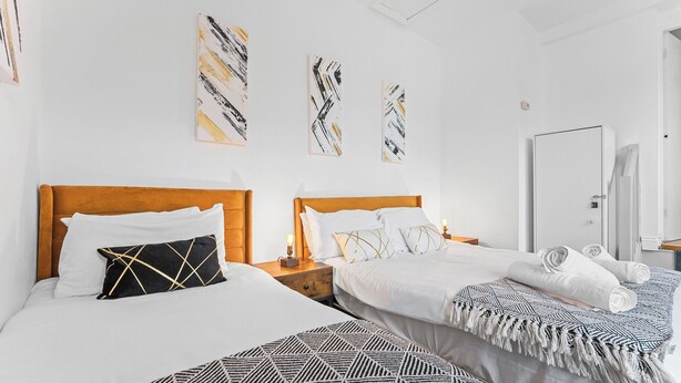 A hotel room with two beds, a wardrobe, and artwork on the wall. - The Hallmark Birmingham Flat (Birmingham)