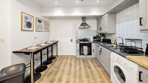 A compact kitchen with a built-in oven, a washing machine, and a dining area with a long table and chairs. - The Hallmark Birmingham Flat (Birmingham)