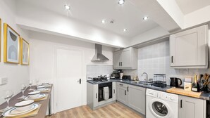 A compact kitchen with a built-in oven, microwave, and washing machine, a dining area with a table set for four, and a white door. - The Hallmark Birmingham Flat (Birmingham)