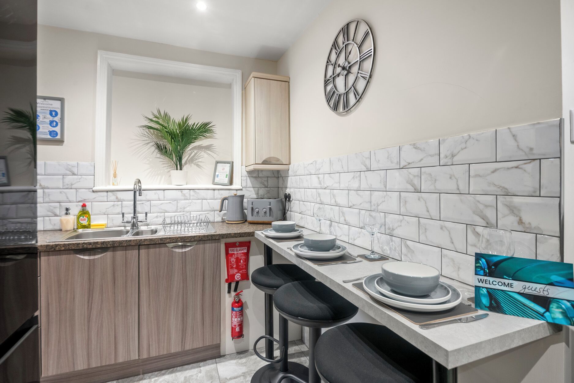 A modern kitchen with a marble backsplash, a clock, bar stools, and a fire blanket.