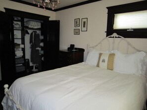 Une chambre à coucher comprenant un lit, une armoire, une table de chevet et une fenêtre avec des stores.