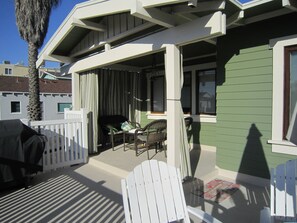 A covered outdoor seating area with chairs and a table, a white picket fence, and a green building facade. - Charming 2-bedroom cottage steps to the Strand Hermosa Beach (Hermosa Beach)