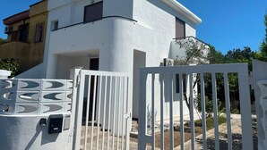 Ein modernes, zweistöckiges Haus mit weißer Fassade, einem verschlossenen Eingangsbereich und einer sichtbaren Treppe zum Eingang.