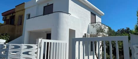 A modern two-story house with a white exterior, a gated entrance, and a visible staircase leading to the entrance.