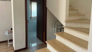 Eine Treppe führt zu einer zweiten Etage, eine Tür zu einem Badezimmer und ein kleiner Tisch mit Gegenständen darauf.