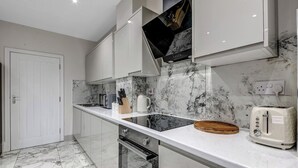 A modern kitchen with a marble backsplash, white cabinetry, and a built-in oven. - Oxford City Stay Cowley House (Oxford)