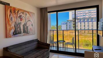 Una sala de estar moderna con un sofá gris, un cuadro y un ventanal con vistas a un hotel y edificios.