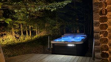 A hot tub in a wooded area with a wooden deck and stone wall.