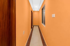 A hallway with orange walls, a wooden door on the left, and a window on the right.