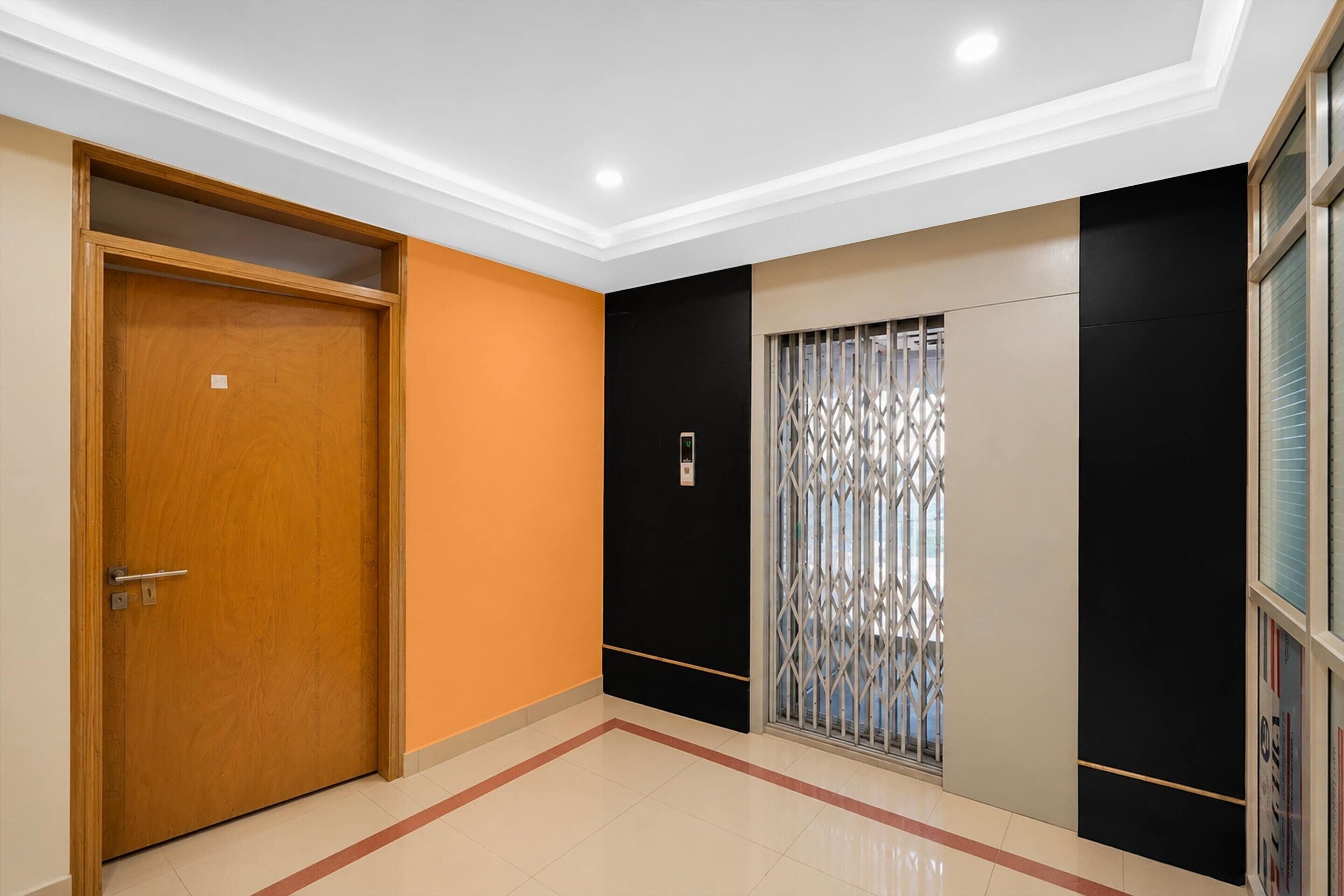 A hallway with a wooden door, a black and beige wall, and a window with a metal grille.