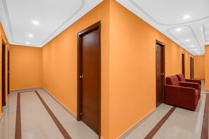 A hotel corridor with orange walls, wooden doors, and a seating area with red upholstered chairs. - Hotel O Bhagalpur Railway Junction 2 (Bhāgalpur)