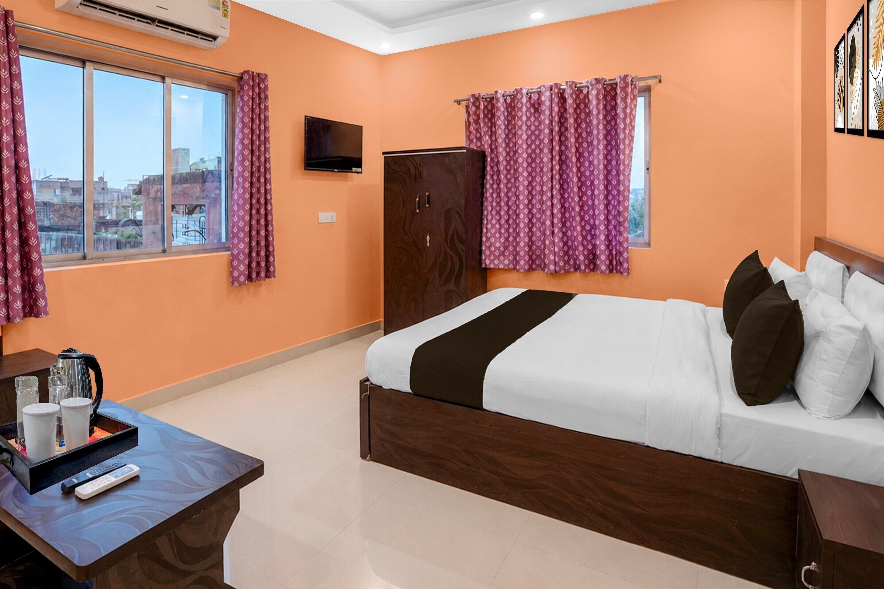 A hotel room with a bed, a desk with a kettle and cups, a TV, and a wardrobe.