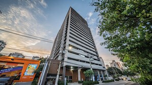 Un moderno edificio de gran altura con una entrada destacada y una señalización visible en la calle que indica un carril para autobuses.