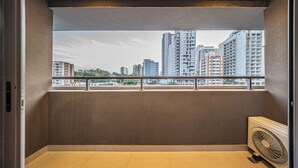 Un balcón con vistas a edificios altos, barandilla y ventilador de pie.
