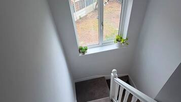 Uma escadaria com uma pequena janela no topo, degraus carpetados e um corrimão branco.