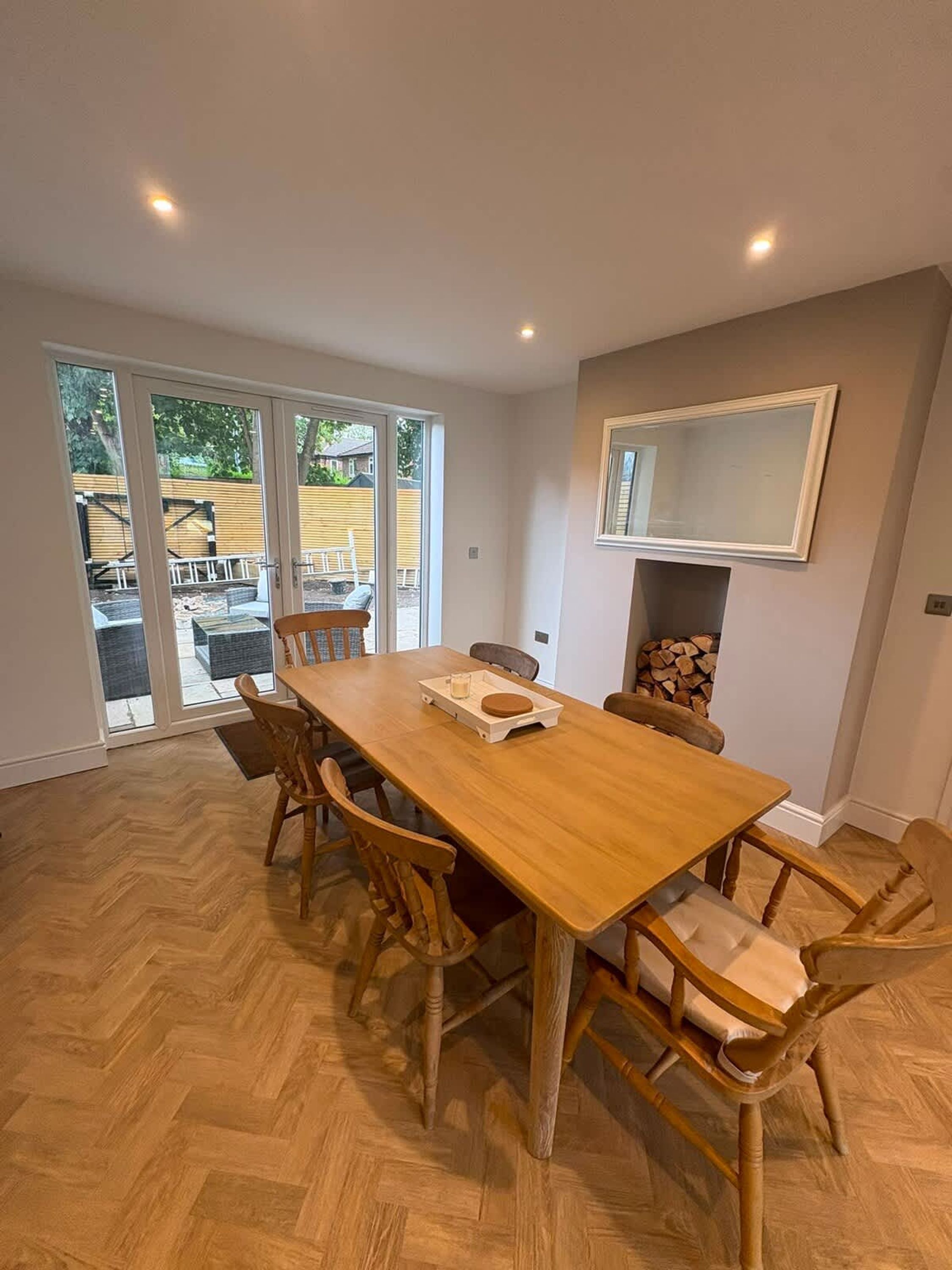 A dining area with a wooden table and chairs, a fireplace, and a view through glass doors.