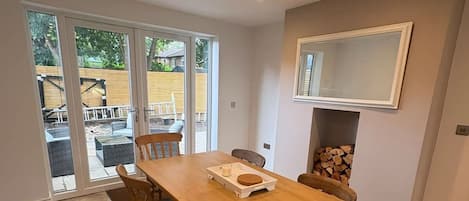 Comedor con mesa y sillas de madera, chimenea y vistas a través de puertas de vidrio.