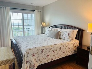 A bedroom with a bed, a window with curtains, a bedside lamp, and a view of the outdoors. - 4BR second-row beach house with private pool, near Holden Beach. (Holden Beach)
