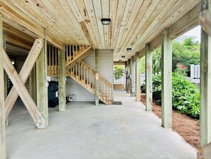 A covered outdoor area with a concrete floor, wooden beams, and a staircase leading to an upper level. - 4BR second-row beach house with private pool, near Holden Beach. (Holden Beach)