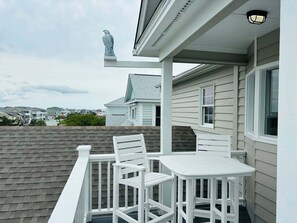 A balcony with white chairs and a table, a bird statue, and a view of other houses. - 4BR second-row beach house with private pool, near Holden Beach. (Holden Beach)