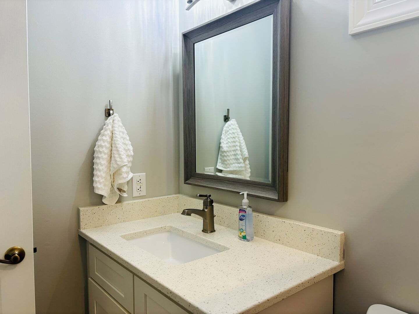 A bathroom with a white sink, a mirror, a towel hanging on a hook, and a bottle of hand soap.