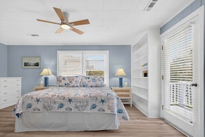 A bedroom with a bed, two bedside tables, a ceiling fan, a window with blinds, and a white wardrobe. - Sea Monkeys Beach Cottage: 3BR, 2BA  retreat in Holden Beach. (Holden Beach)