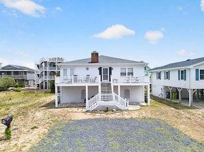 A two-story house with a front porch and a staircase leading to the entrance. - Sea Monkeys Beach Cottage: 3BR, 2BA retreat in Holden Beach. (Holden Beach)