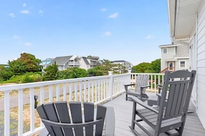 A wooden deck with two Adirondack chairs and a fire pit, overlooking a residential area with houses and greenery. - Sea Monkeys Beach Cottage: 3BR, 2BA  retreat in Holden Beach. (Holden Beach)