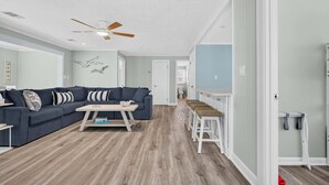 A spacious living room with a sectional sofa, a coffee table, and a ceiling fan. - Sea Monkeys Beach Cottage: 3BR, 2BA  retreat in Holden Beach. (Holden Beach)