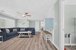 A spacious living room with a sectional sofa, a coffee table, and a ceiling fan. - Sea Monkeys Beach Cottage: 3BR, 2BA  retreat in Holden Beach. (Holden Beach)