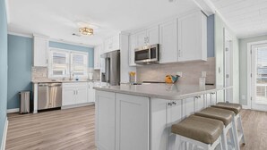 A modern kitchen with white cabinetry, stainless steel appliances, and a central island with bar stools. - Sea Monkeys Beach Cottage: 3BR, 2BA  retreat in Holden Beach. (Holden Beach)