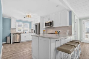 A modern kitchen with white cabinetry, stainless steel appliances, and a central island with bar stools. - Sea Monkeys Beach Cottage: 3BR, 2BA  retreat in Holden Beach. (Holden Beach)