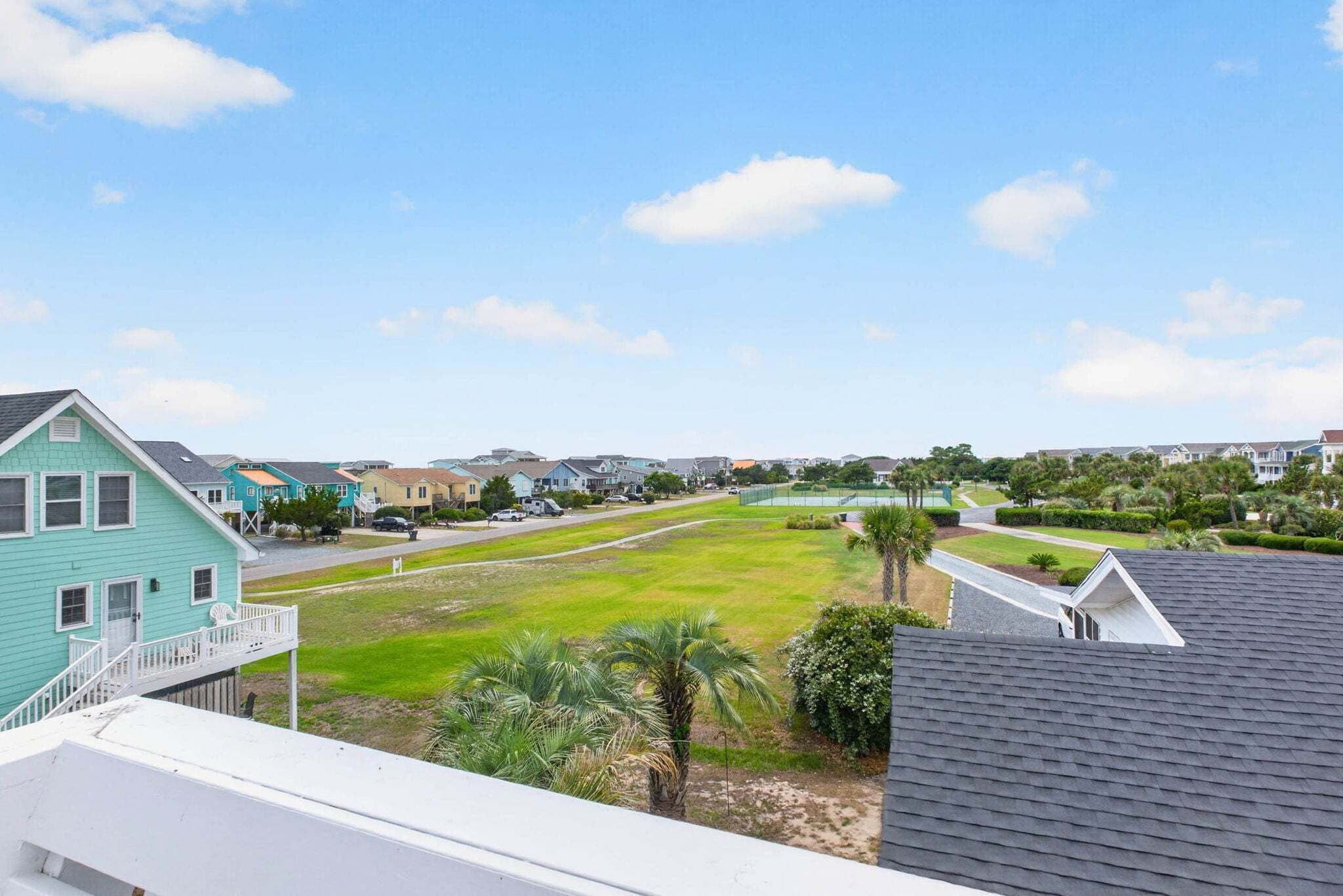 Un barrio residencial con casas, un campo verde y una cancha de tenis.