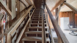 A wooden staircase leading to an upper floor, with a modern chair and a white appliance on the landing. - Sea Monkeys Beach Cottage: 3BR, 2BA  retreat in Holden Beach. (Holden Beach)