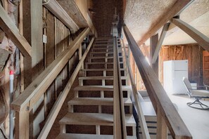 A wooden staircase leading to an upper floor, with a modern chair and a white appliance on the landing. - Sea Monkeys Beach Cottage: 3BR, 2BA  retreat in Holden Beach. (Holden Beach)