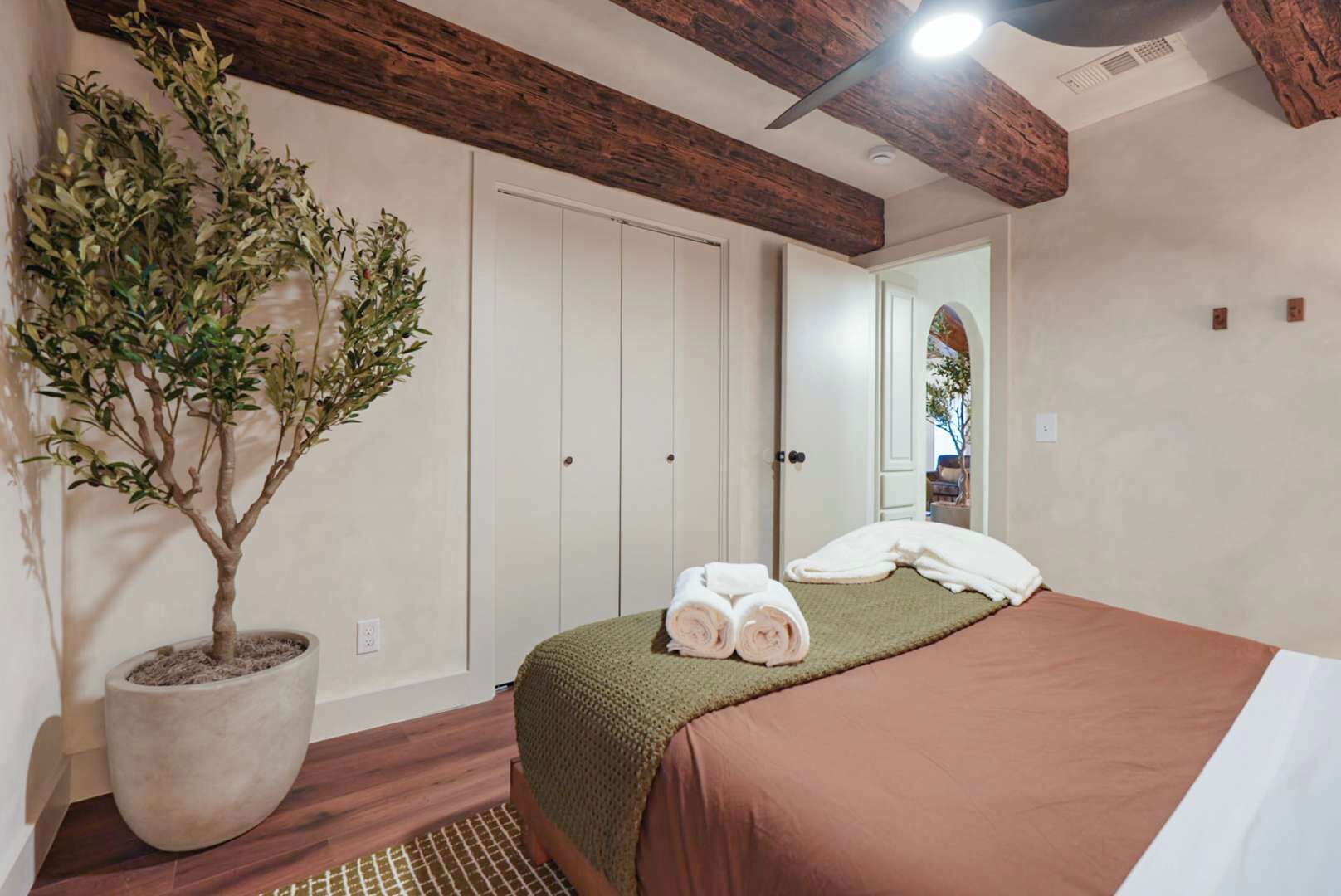 Un dormitorio con una cama, una planta en maceta y una puerta que da a otra habitación.