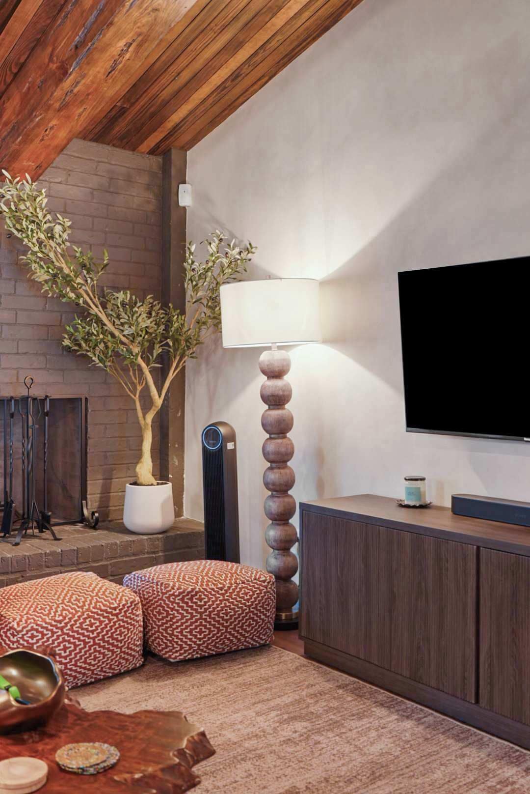Una sala de estar moderna con chimenea, un televisor de pantalla plana grande, una lámpara de pie alta y otomanas estampadas.