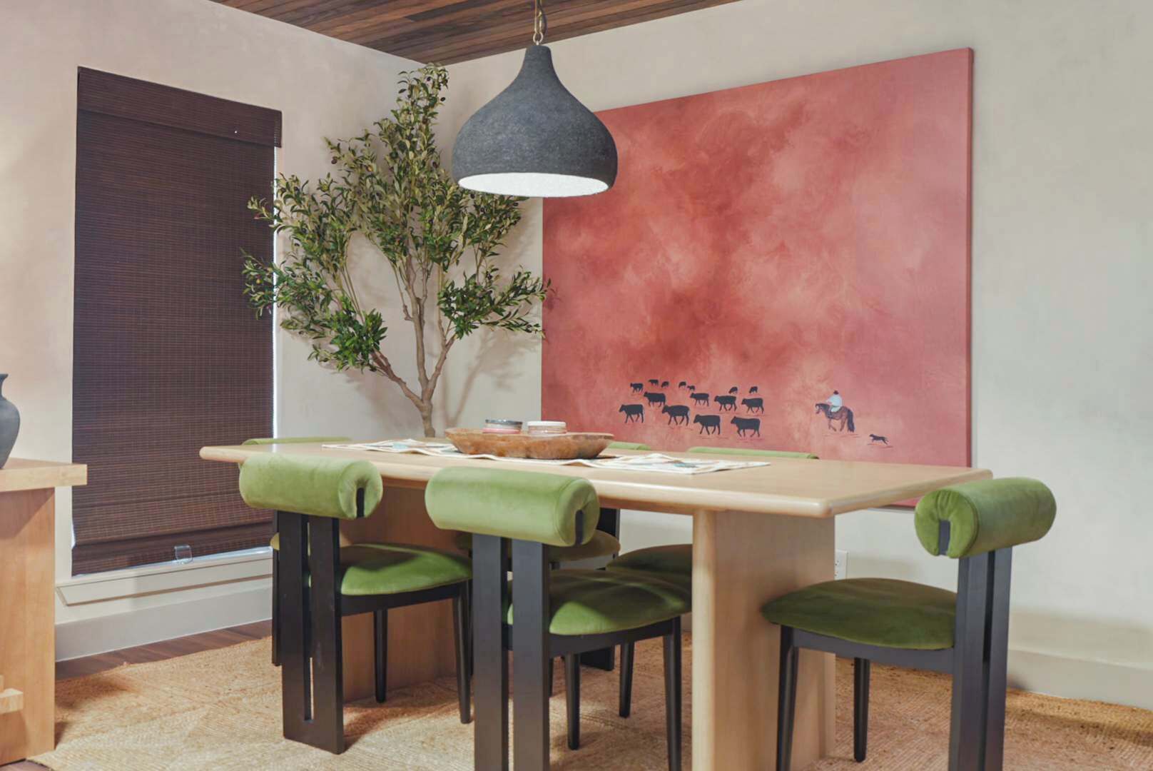 Un comedor con una mesa, sillas, una lámpara colgante, un cuadro grande en la pared y una planta en maceta.