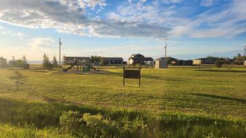 A grassy field with a playground, a small shelter, and residential buildings in the background.