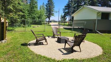 An outdoor seating area with chairs and a table, surrounded by a fence and trees.