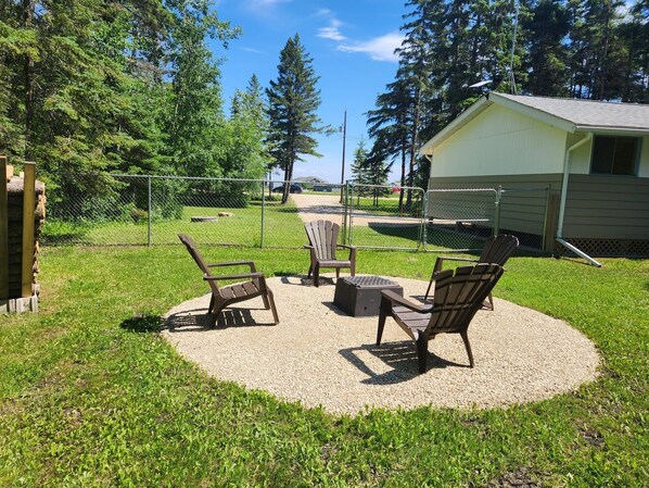 An outdoor seating area with chairs and a table, surrounded by a fence and trees.