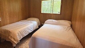 A room with two single beds, wooden walls, a ceiling fan, and a window with a view of trees. - Modern Rustic Cabin in Balaton Beach with Lake Access & Firepit (Balaton Beach)