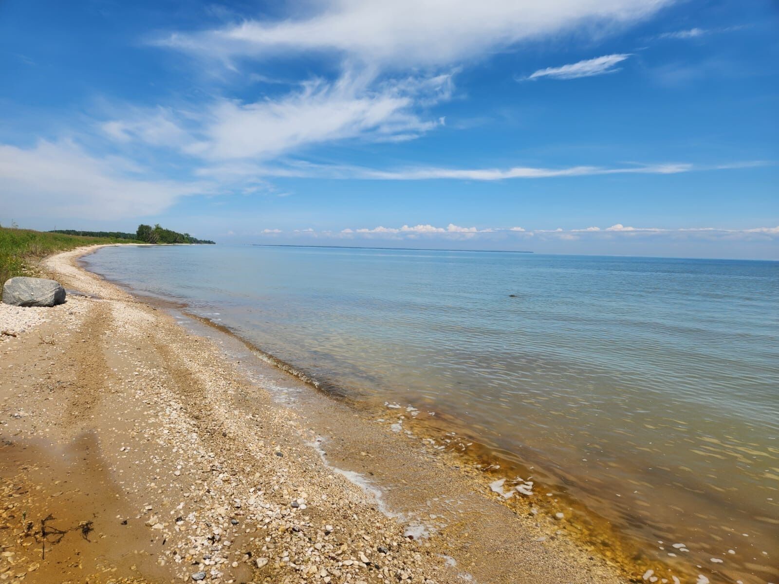 A beach with clear water, pebbles, and a distant shoreline.