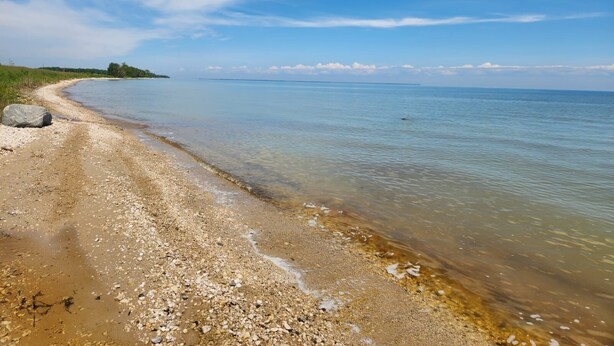 A beach with clear water, pebbles, and a distant shoreline. - Modern Rustic Cabin in Balaton Beach with Lake Access & Firepit (Balaton Beach)