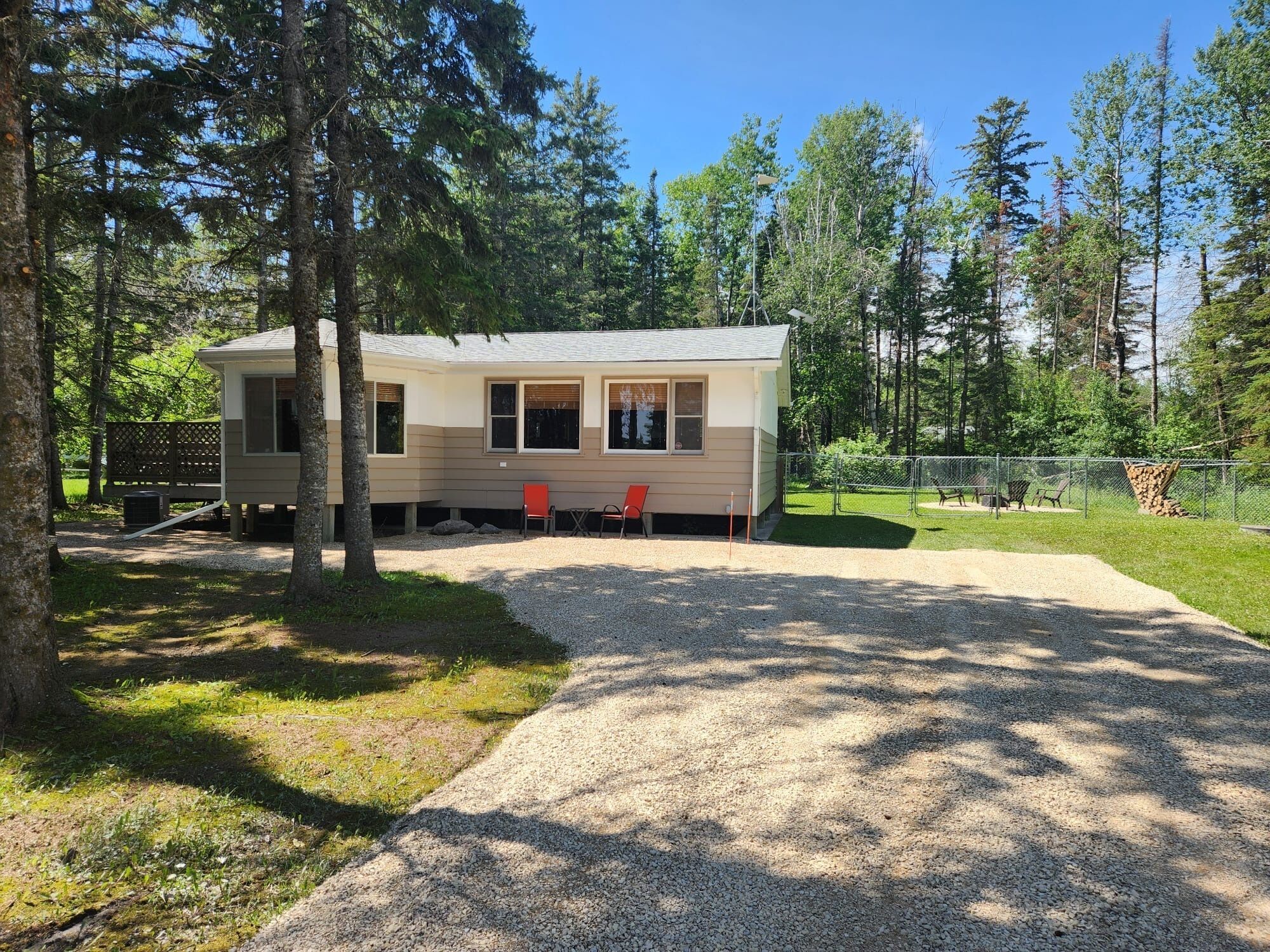 A single-story cabin with a gravel driveway, surrounded by trees.