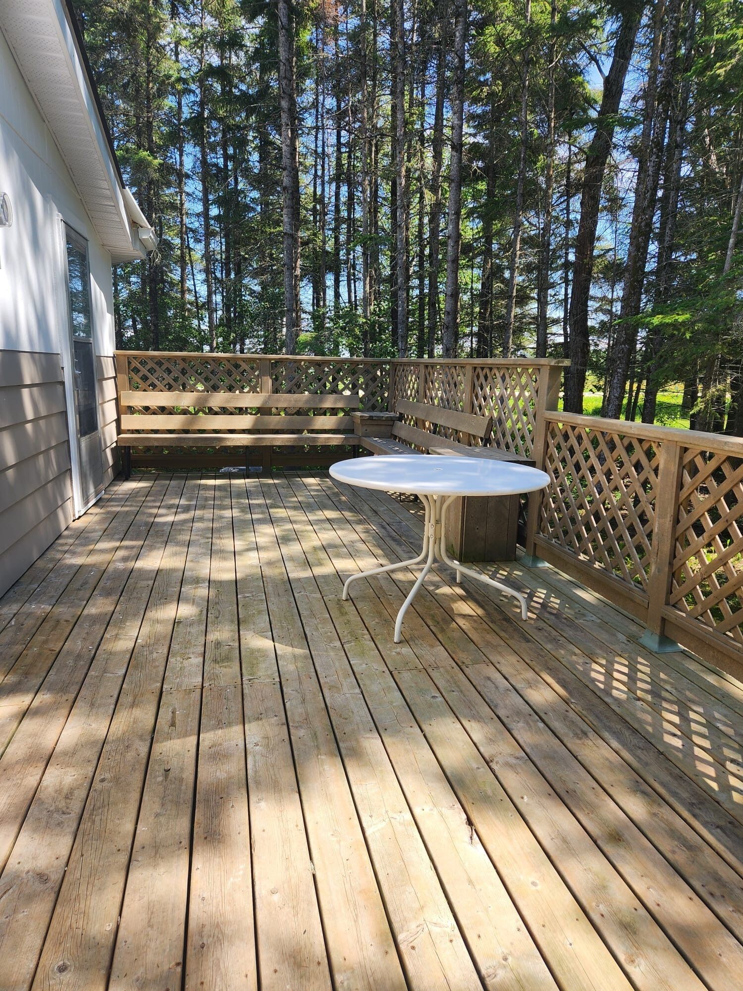 A wooden deck with a table and benches, surrounded by a wooden fence and tall trees.